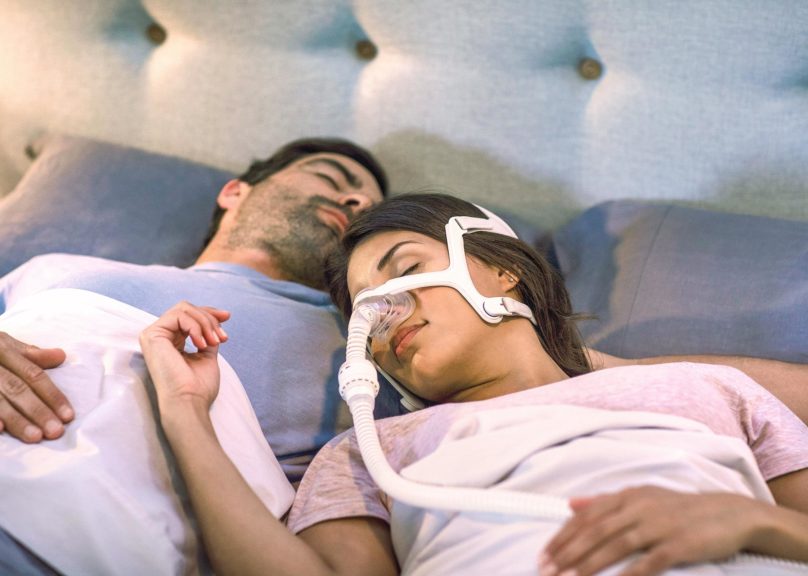Tummahiuksinen pariskunta nukkuu sängyssä ja naisella on CPAP-laitteet.