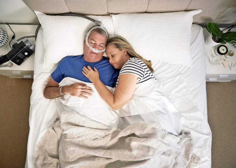 Keski-ikäinen pariskunta nukkuu sängyssä ja miehellä on CPAP-laitteet.