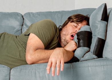 Mies nukkuu sohvalla käsi sohvalta roikkuen.