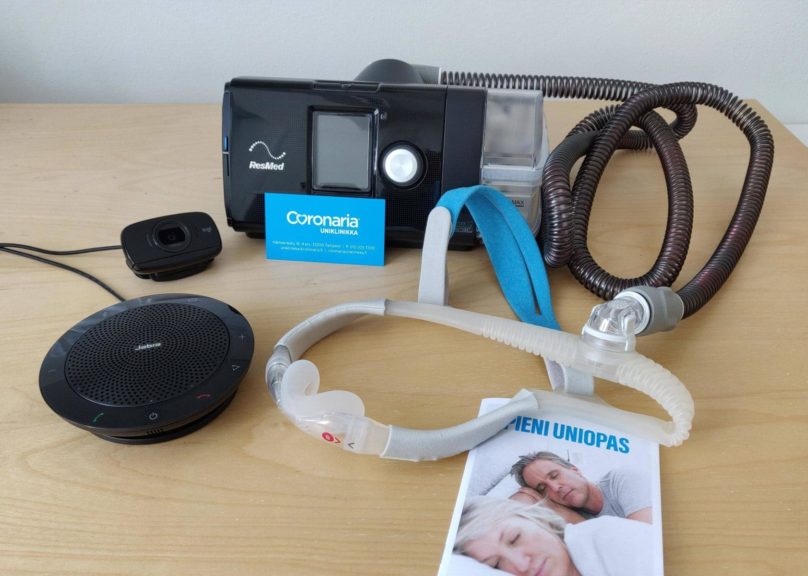Pöydällä Resmedin CPAP-laite, maski ja pieni uniopas