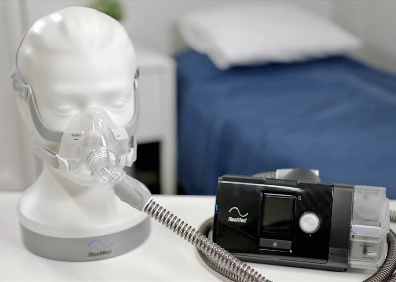 Resmedin CPAP-laite pöydällä ja maski nuken päässä.