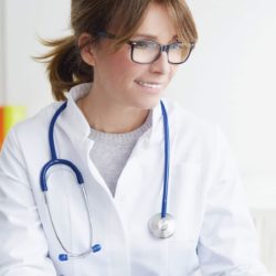 Ruskeahiuksinen naislääkäri ja naispotilas istuvat pöydän ääressä lääkärin käyttäessä kannettavaa tietokonetta.