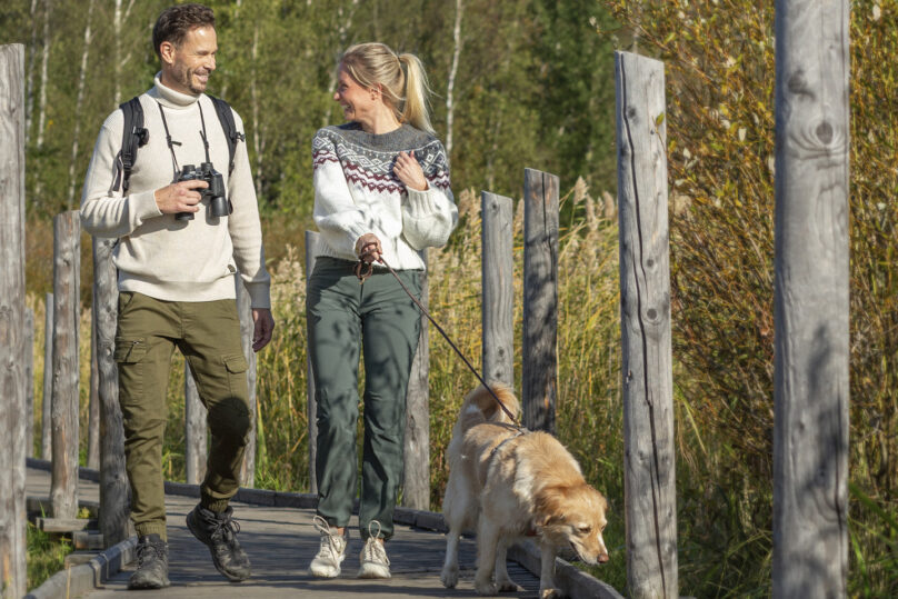 nainen ja mies retkeilevät koiran kanssa pitkospuilla