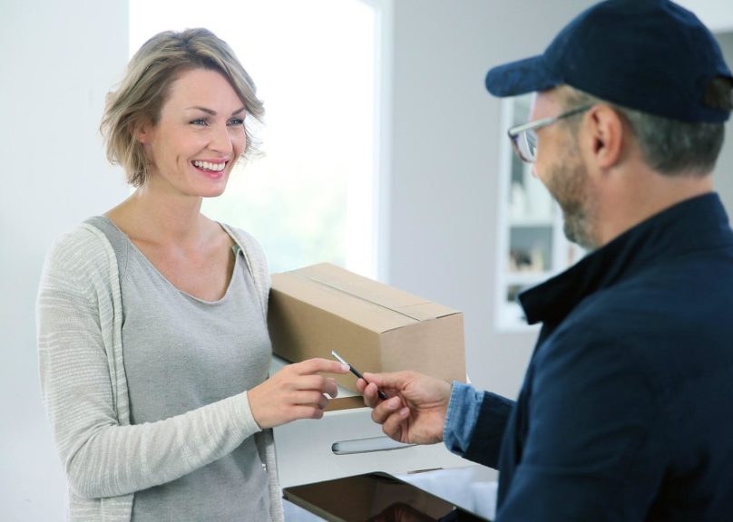 Vaaleahiuksinen nainen vastaanottaa kotiin paketin.
