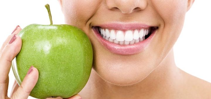 Hymyilevä nainen pitää kädessään vihreää omenaa suunsa vieressä.