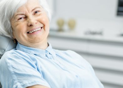 seniori nainen hymyilee ja istuu hammaslaakarissa tuolissa