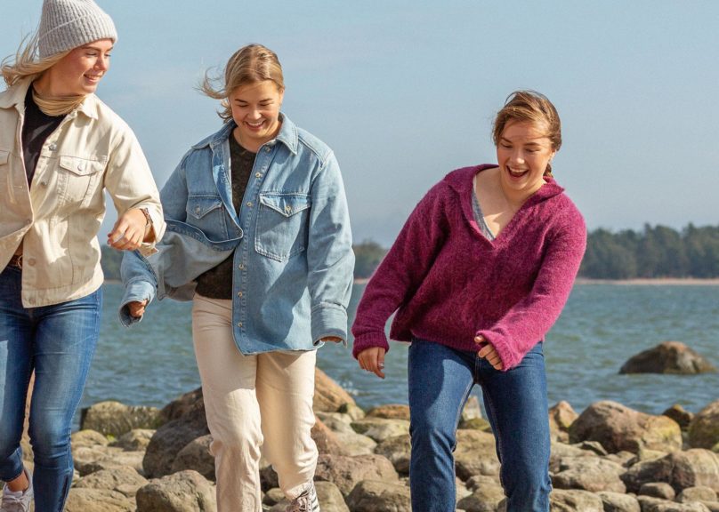 kolme nuorta naista kavelevat rannalla ja hymyilevat