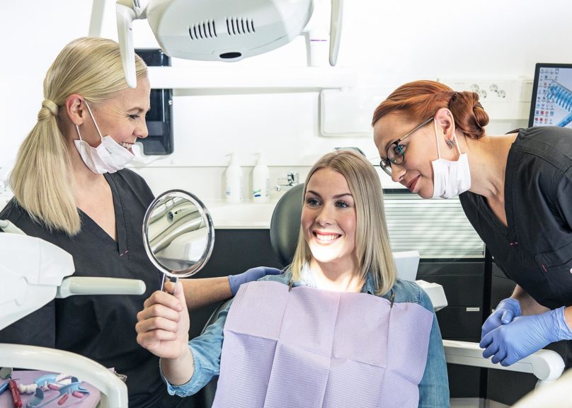 Kaksi hammaslääkäriä ja naisasiakas katsovat yhdessä peilistä työn tulosta.