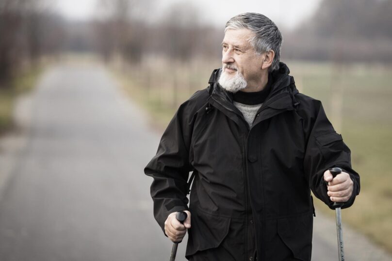 Vanhempi mies sauvakävelee ulkona syksyllä.