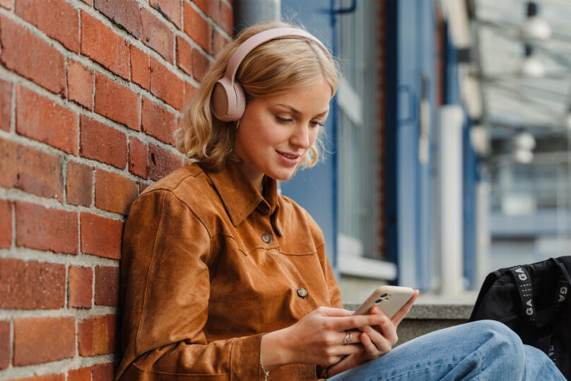 nuori nainen nojaa tiiliseinään kuulokkeet päässä