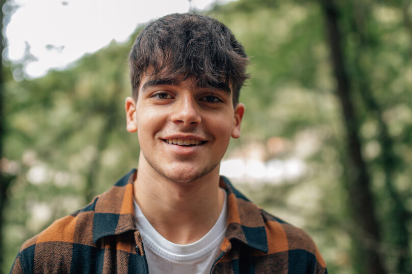 Nuori mies hymyilee ja katsoo kameraan ulkona